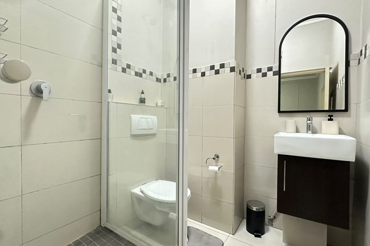 A compact bathroom featuring a wall-mounted toilet, a glass-enclosed shower, and a modern vanity unit with a basin and mirror.