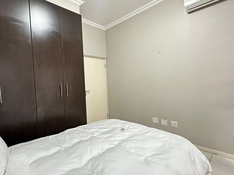 A bedroom featuring dark wood built-in cupboards, crown molding, and a wall-mounted air conditioning unit.