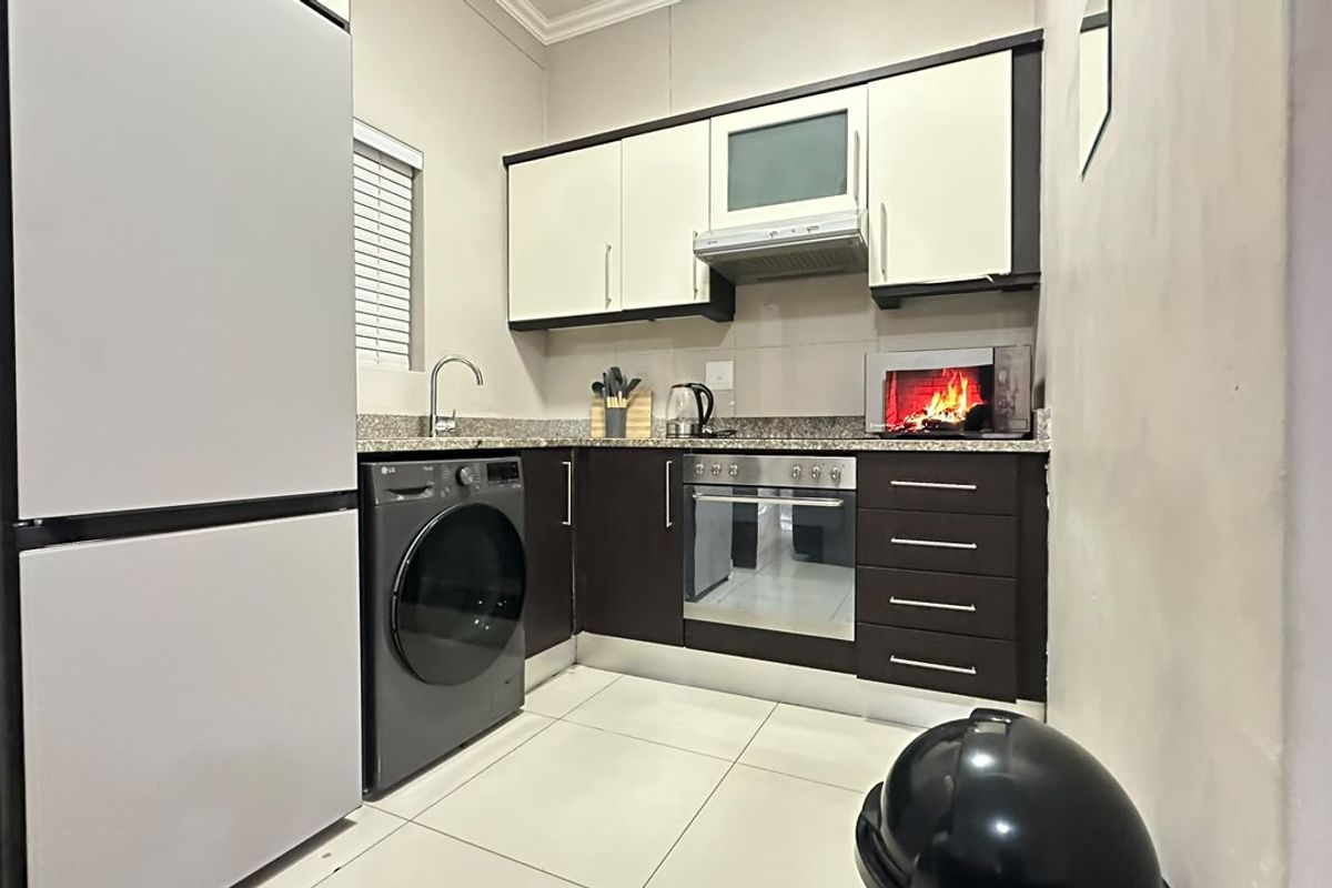 A compact, modern kitchen featuring dark and light cabinetry, granite countertops, integrated appliances, and tiled flooring.
