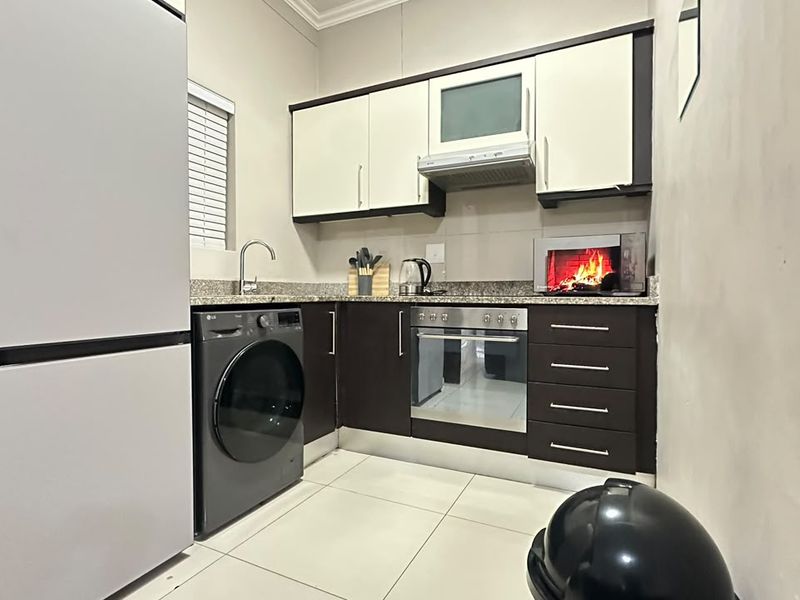 A compact, modern kitchen featuring dark and light cabinetry, granite countertops, integrated appliances, and tiled flooring.