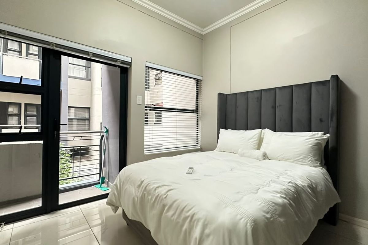 A well-maintained bedroom featuring tiled flooring, modern aluminium window frames, and direct access to a private balcony through a sliding door.