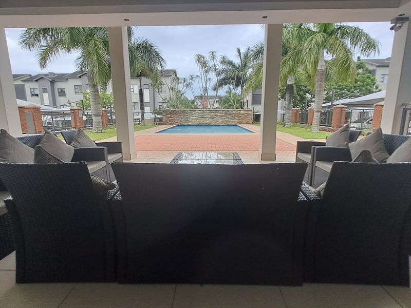 A covered patio area overlooking a swimming pool with a stone feature wall and brick paved surrounds.