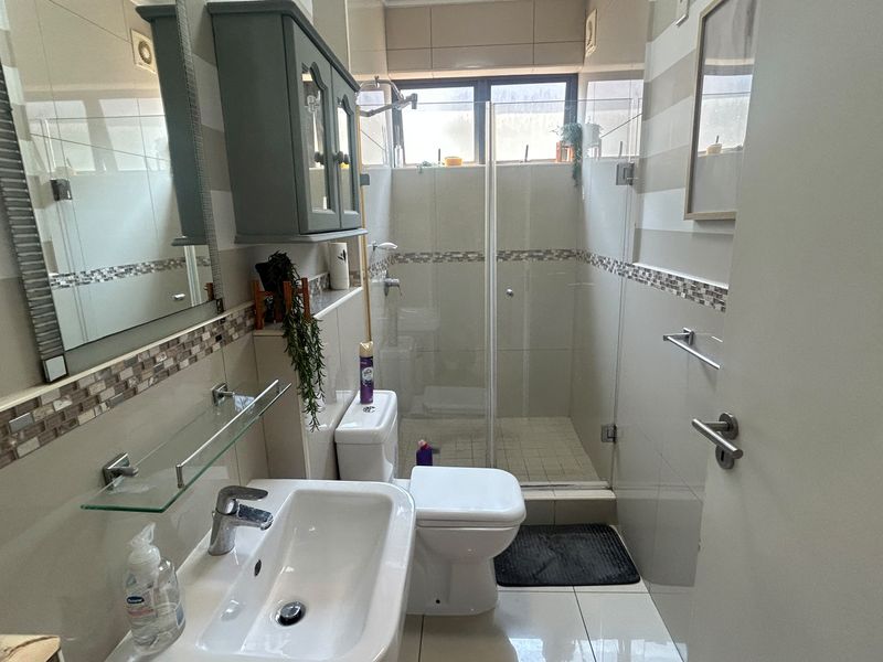 A functional bathroom featuring a glass-enclosed shower, wall-mounted vanity cabinet, ceramic basin, and neutral tiled finishes throughout.