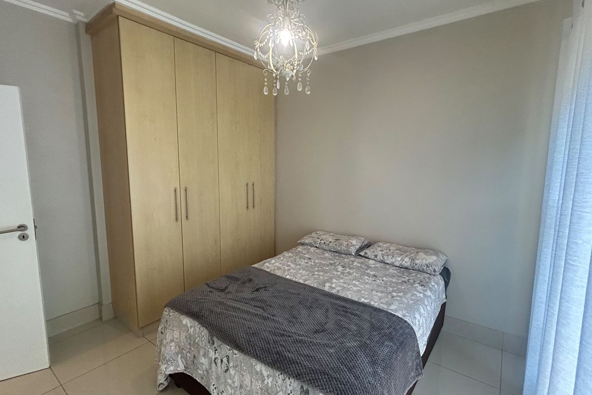 A well-maintained bedroom featuring light-toned built-in wardrobes, tiled flooring, and a decorative chandelier, offering a clean and functional living space.