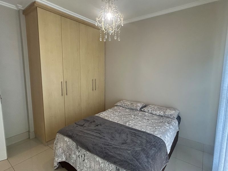 A well-maintained bedroom featuring light-toned built-in wardrobes, tiled flooring, and a decorative chandelier, offering a clean and functional living space.