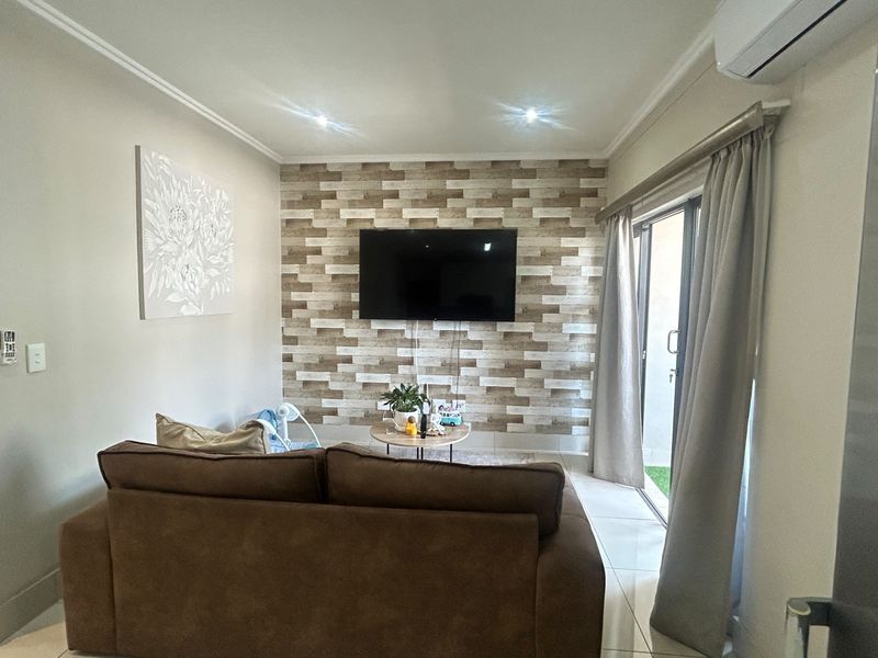A well-maintained living room featuring a textured feature wall, tiled flooring, recessed lighting, and a sliding glass door providing access to the outdoor area.