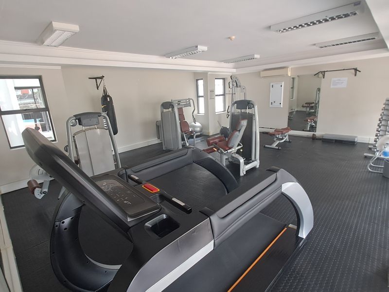 A functional apartment gym facility featuring rubber flooring, mirrored walls, and integrated air conditioning for a comfortable workout environment.