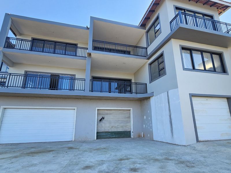 Front elevation of a multi-level apartment building featuring three garage doors, multiple balconies with metal railings, and a concrete driveway.