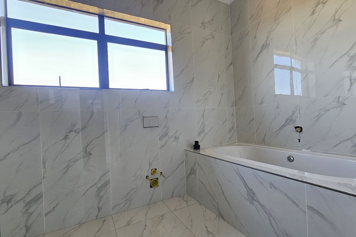 A modern, unfinished bathroom featuring marble-look porcelain tiling throughout, a built-in bathtub, and plumbing rough-ins ready for final fixture installation.