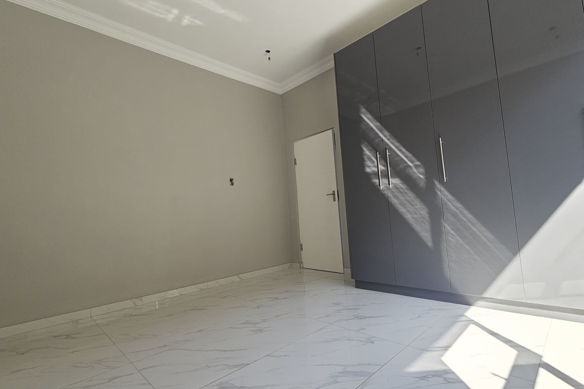 A bright, modern bedroom featuring high-gloss grey built-in cupboards, elegant marble-look floor tiles, and crisp crown molding throughout the space.