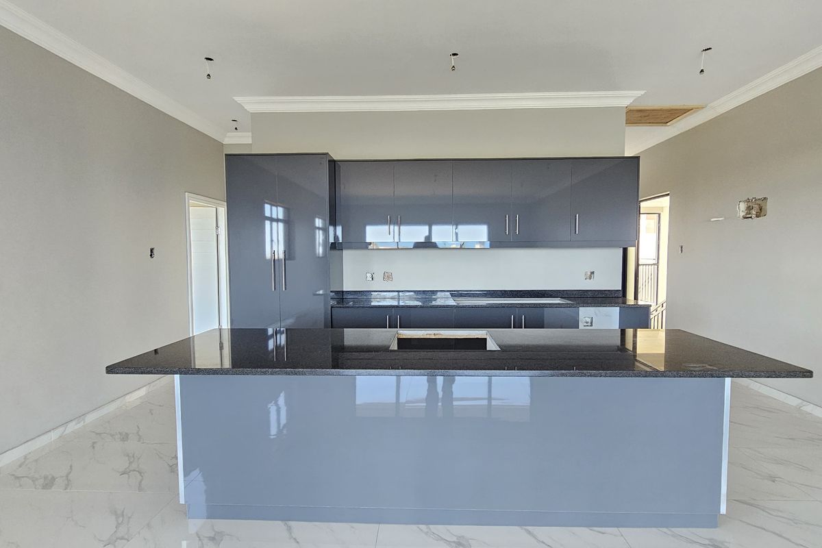 Modern kitchen featuring sleek grey cabinetry, granite countertops, a central island, and elegant marble-look floor tiles in an open-plan layout.