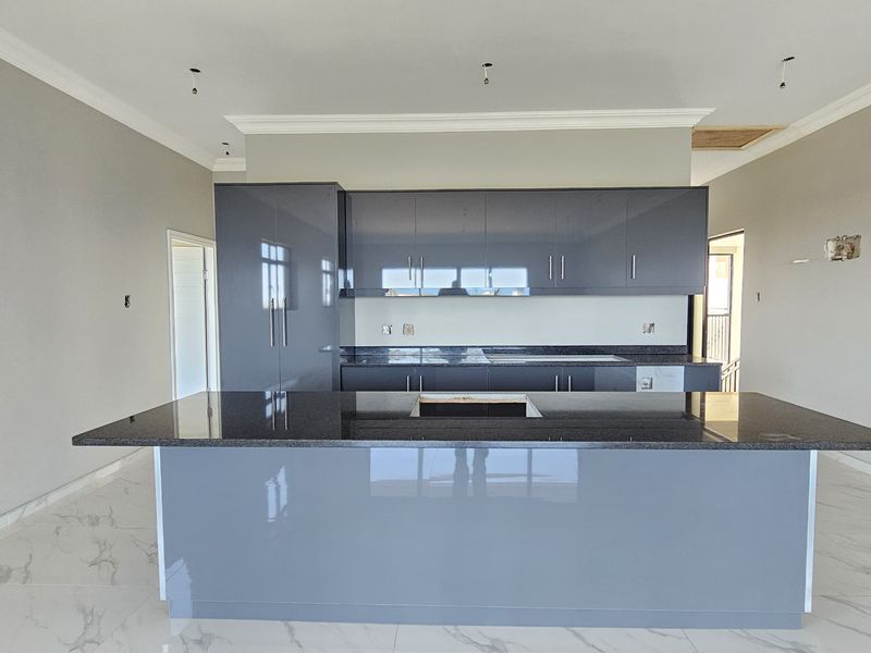Modern kitchen featuring sleek grey cabinetry, granite countertops, a central island, and elegant marble-look floor tiles in an open-plan layout.