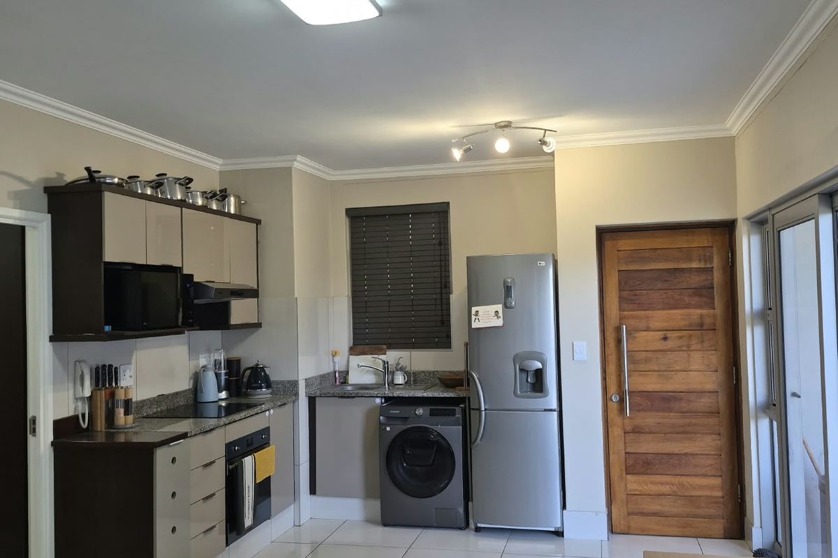 A functional kitchen featuring modern cabinetry, granite countertops, integrated appliances, and tiled flooring, with direct access to an exterior door.
