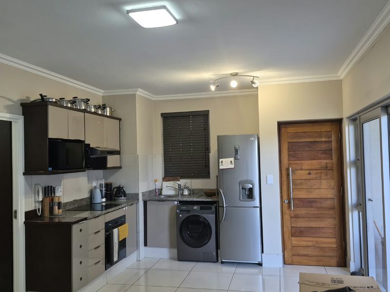 A functional kitchen featuring modern cabinetry, granite countertops, integrated appliances, and tiled flooring, with direct access to an exterior door.