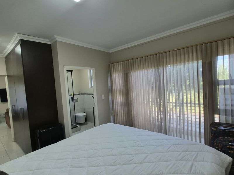 Spacious bedroom featuring built-in cupboards, tiled flooring, and large sliding glass doors leading to an outdoor area, with an attached en-suite bathroom.