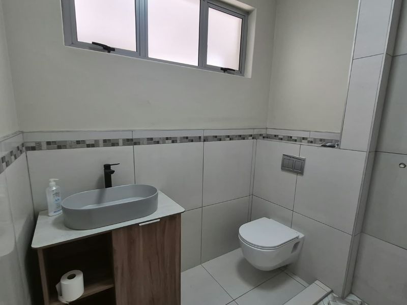 A modern bathroom featuring a wall-mounted toilet, a contemporary vanity with a vessel sink, and neutral tiled finishes throughout.