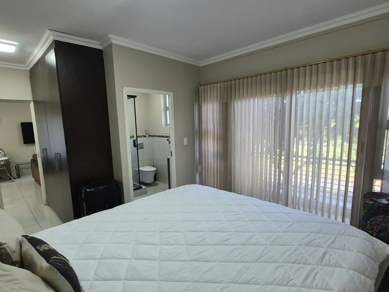 Spacious bedroom featuring built-in cupboards, tiled flooring, and an en-suite bathroom, with large sliding doors providing access to an outdoor area.