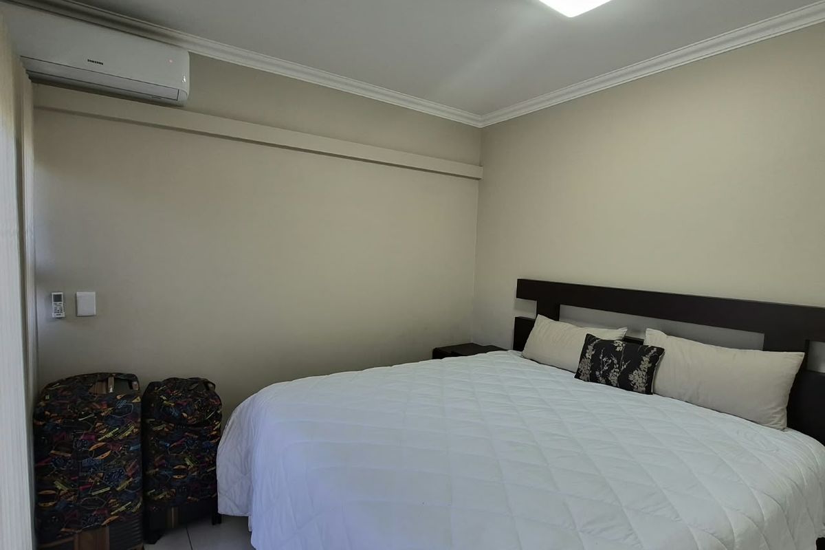 A well-maintained bedroom featuring tiled flooring, crown molding, and a wall-mounted air conditioning unit.