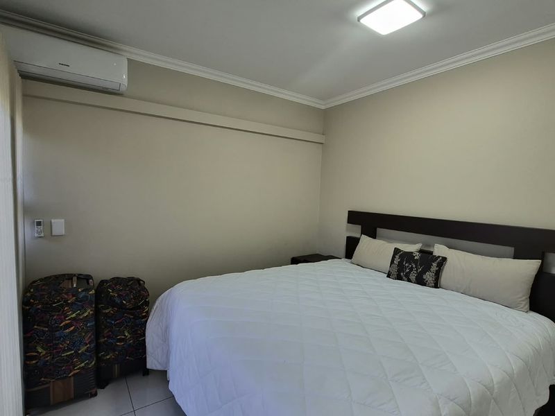 A well-maintained bedroom featuring tiled flooring, crown molding, and a wall-mounted air conditioning unit.