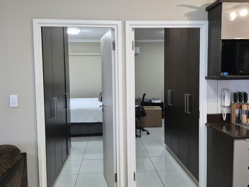 A functional hallway featuring built-in cupboards, connecting the kitchen area to the bedroom and office spaces with clean tiled flooring throughout.