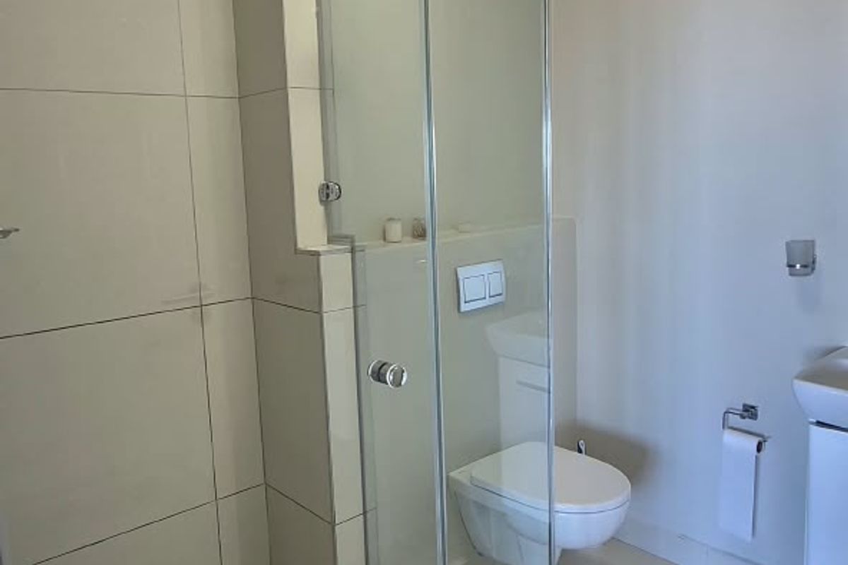 Modern bathroom featuring a glass-enclosed shower, wall-mounted toilet with concealed cistern, and neutral floor-to-ceiling tiling.