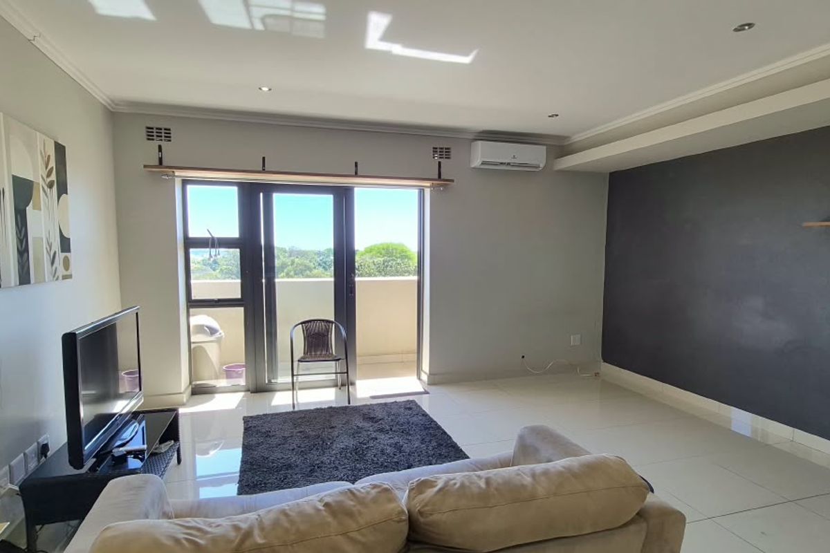 A bright living room featuring tiled floors, an accent wall, a wall-mounted air conditioning unit, and sliding glass doors leading to a balcony.