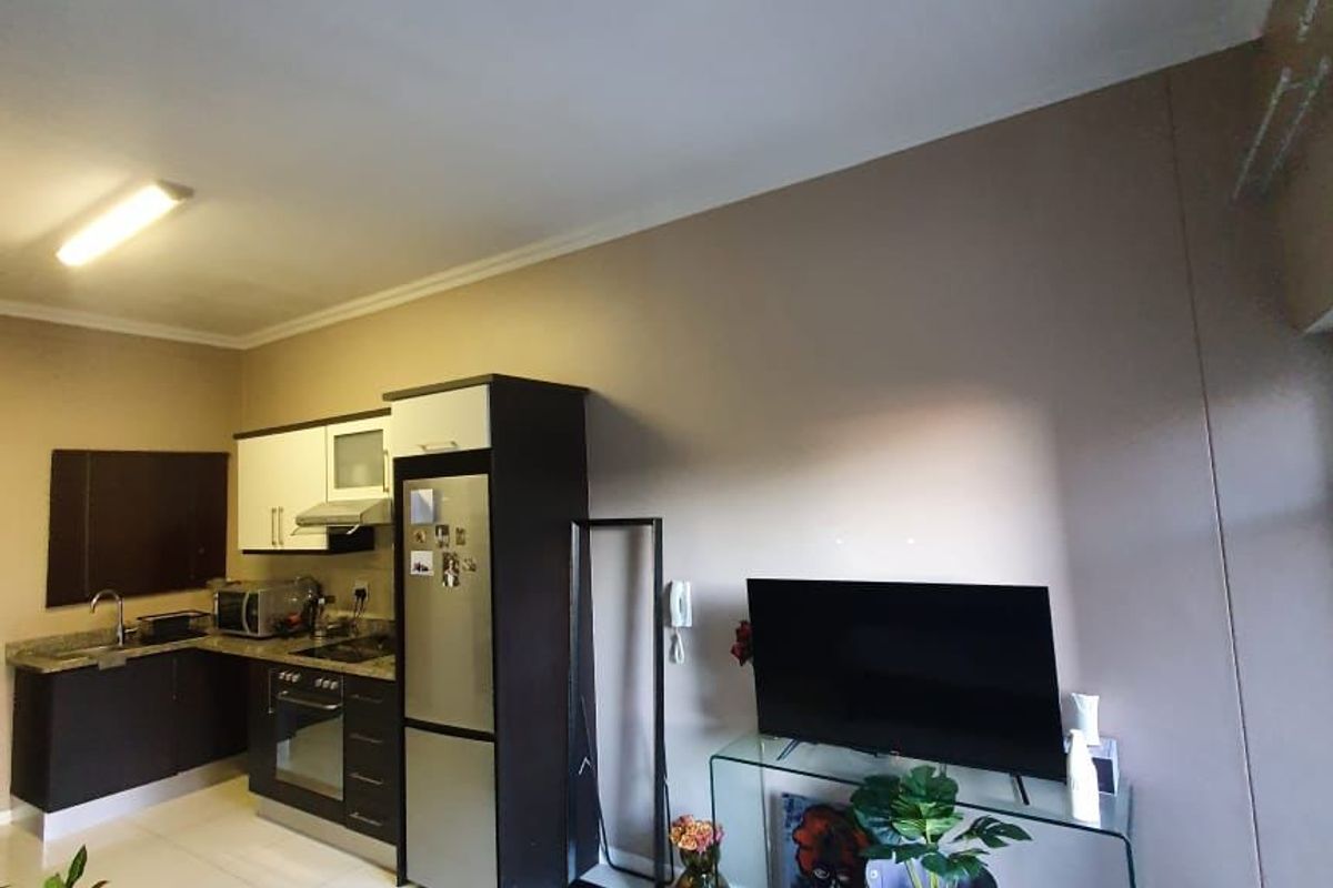 Open-plan living area featuring a compact kitchen with built-in cabinetry, granite countertops, and tiled flooring throughout.