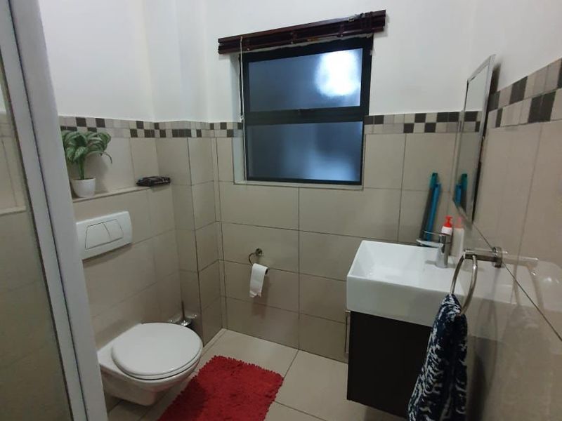 A modern bathroom featuring a wall-hung toilet, a sleek wall-mounted vanity with basin, and neutral tiled finishes throughout.