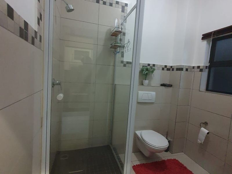 A functional bathroom featuring a glass-enclosed shower, wall-mounted toilet with concealed cistern, and neutral tiled finishes throughout.