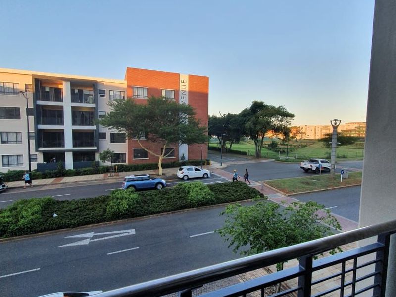 A view from a balcony overlooking a street and surrounding residential buildings.