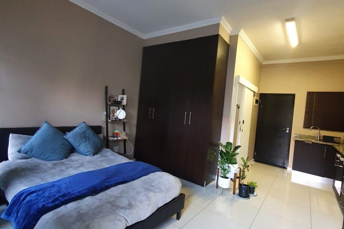 Open-plan studio apartment featuring tiled flooring, built-in cupboards, and a compact kitchenette area with a sink.