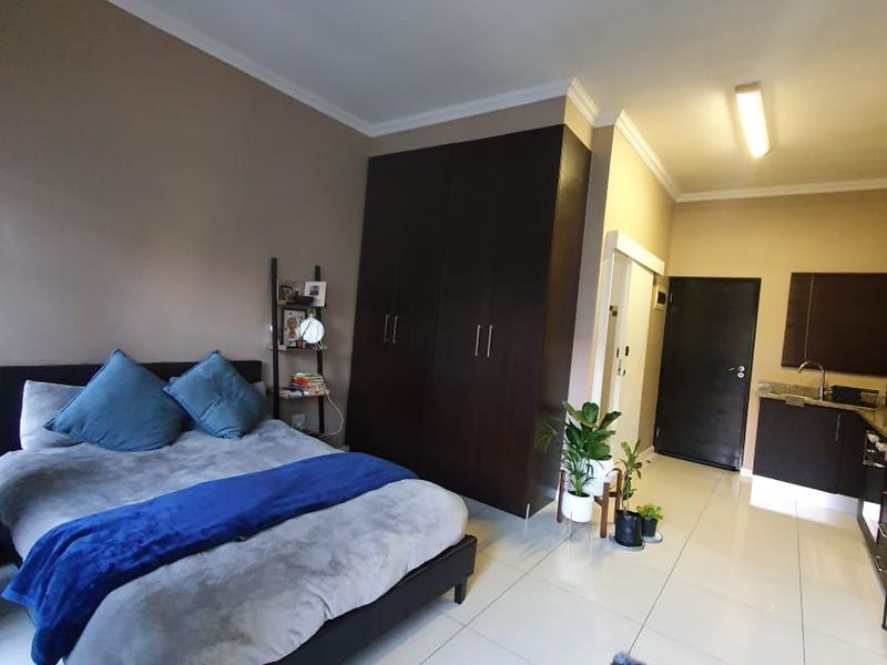 Open-plan studio apartment featuring tiled flooring, built-in cupboards, and a compact kitchenette area with a sink.