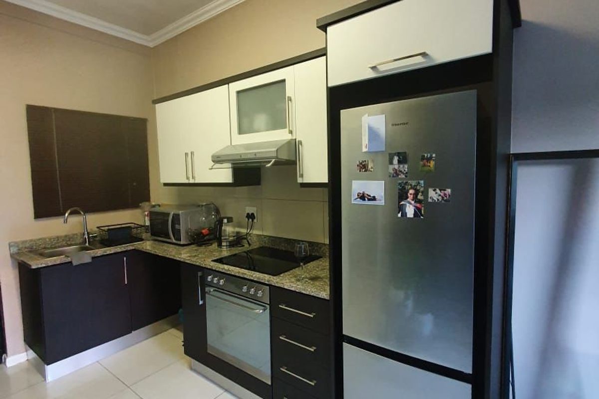 A functional kitchen featuring granite countertops, built-in cabinetry, a stainless steel sink, and integrated appliances including an oven and hob.