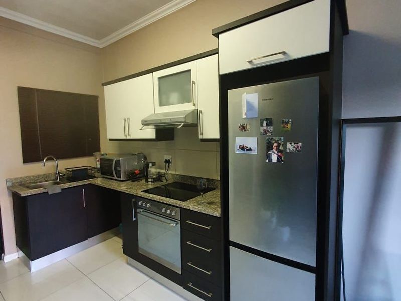 A functional kitchen featuring granite countertops, built-in cabinetry, a stainless steel sink, and integrated appliances including an oven and hob.