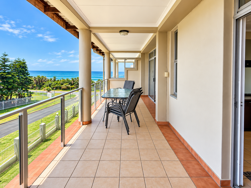 Spacious covered balcony featuring tiled flooring, a modern glass balustrade, and expansive ocean views, providing an ideal outdoor living and entertainment space.