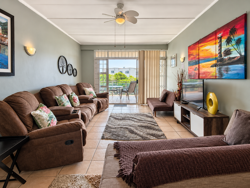 A comfortable living room featuring tiled flooring, a ceiling fan, and a sliding glass door that opens onto a balcony.