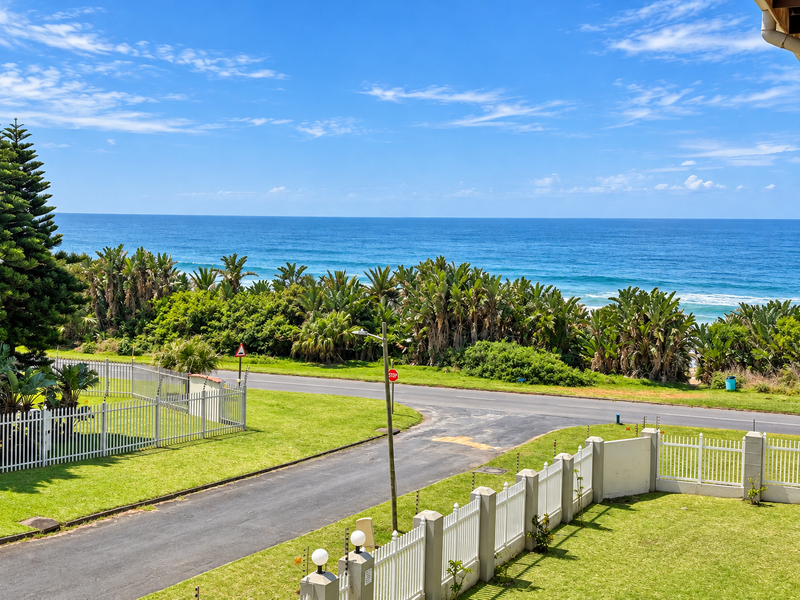 A scenic elevated view overlooking the ocean, featuring a well-maintained lawn, perimeter fencing, and a coastal road.
