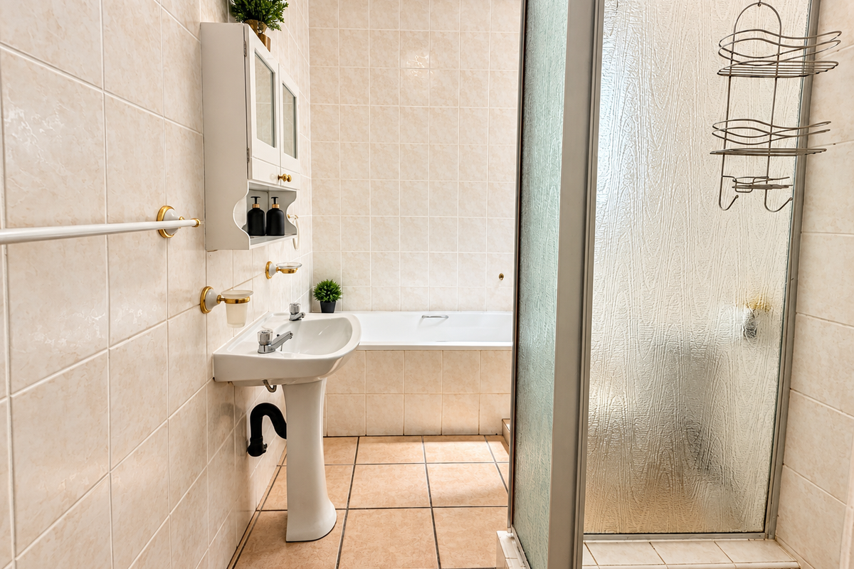 A functional bathroom featuring a pedestal washbasin, a built-in bathtub, and a separate shower enclosure with tiled finishes throughout.