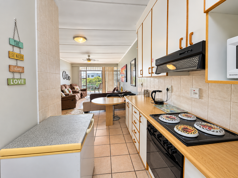 Open-plan kitchen and living area featuring tiled flooring, wooden cabinetry, and integrated cooking appliances, leading to a balcony with natural light.