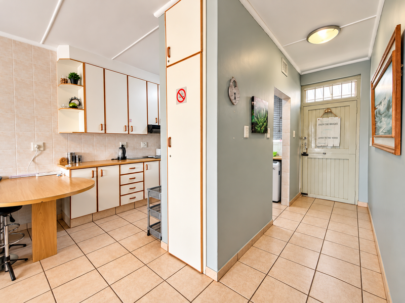 A functional kitchen featuring built-in cabinetry, tiled flooring, and a breakfast counter, leading directly to the apartment entrance.