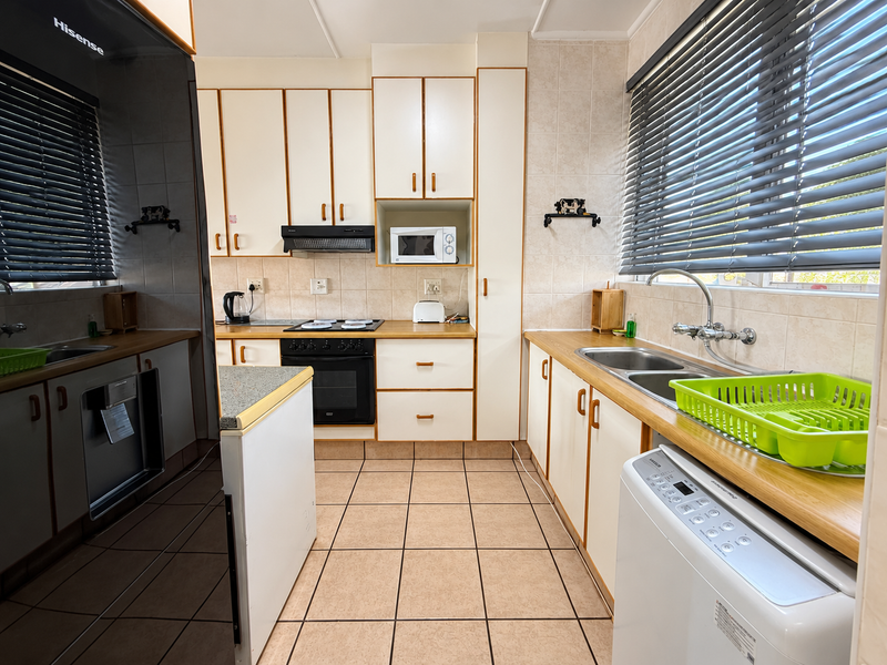 A functional kitchen featuring built-in cabinetry, laminate countertops, a double bowl sink, and integrated cooking appliances with tiled finishes throughout.