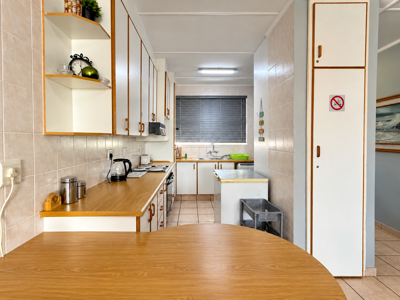 A functional galley-style kitchen featuring laminate countertops, tiled backsplash, ample built-in cabinetry, and a dedicated pantry area.