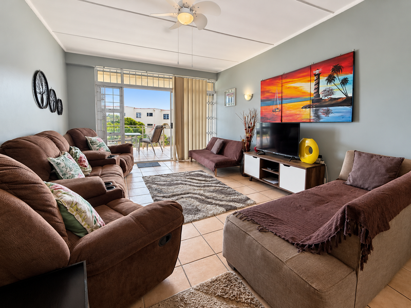 A comfortable living room featuring tiled flooring, a ceiling fan, and a sliding glass door that opens onto a balcony.