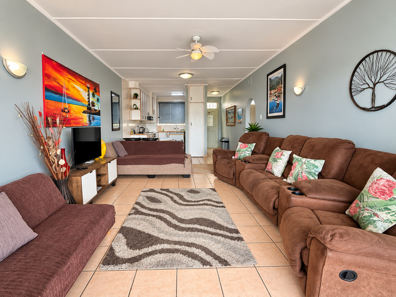 Open-plan living area featuring tiled flooring, a ceiling fan, and a connected kitchen space with built-in cabinetry.