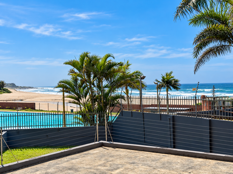 A scenic coastal view overlooking the beach and ocean, featuring a swimming pool and secure boundary wall with electric fencing.