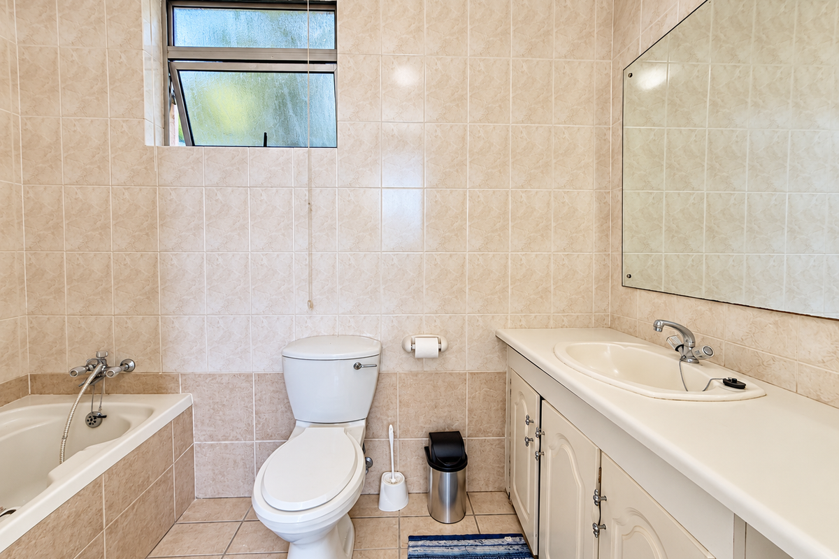 A functional bathroom featuring a built-in bathtub, a vanity unit with an integrated sink, and full-height wall tiling.