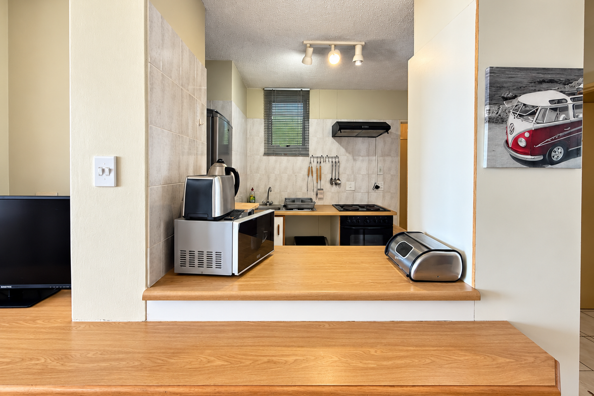 A functional kitchen featuring a wooden breakfast bar, built-in oven, electric hob, extractor fan, and tiled backsplash, offering a practical layout for daily use.