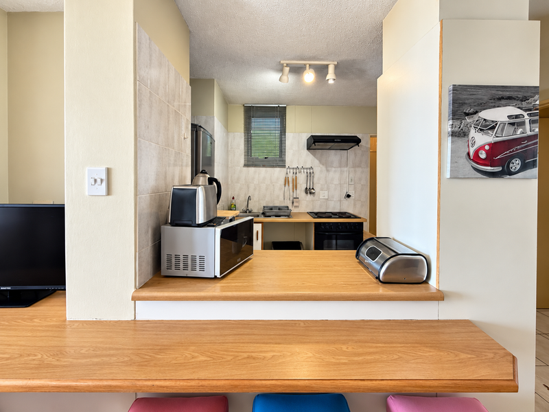 A functional kitchen featuring a wooden breakfast bar, built-in oven, electric hob, extractor fan, and tiled backsplash, offering a practical layout for daily use.