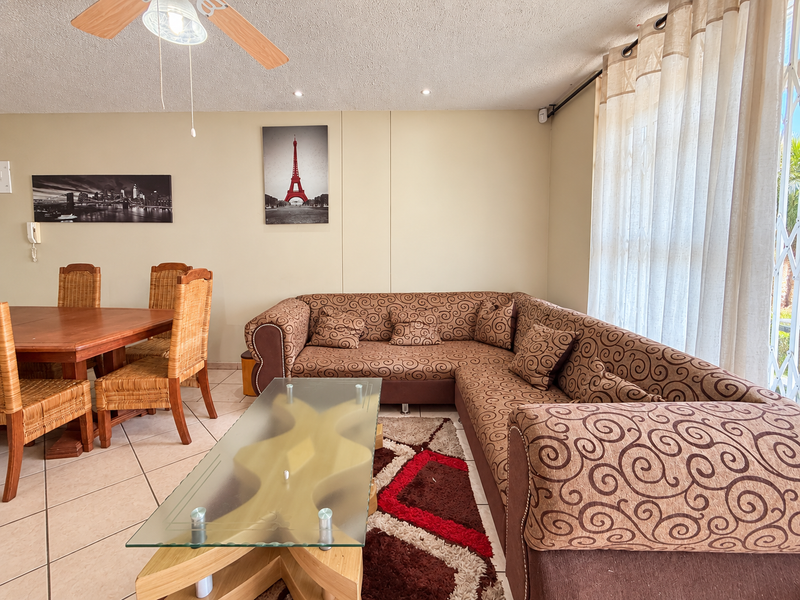 Open-plan living and dining area featuring tiled flooring, recessed lighting, and a ceiling fan, with direct access to an outdoor area via a security gate.