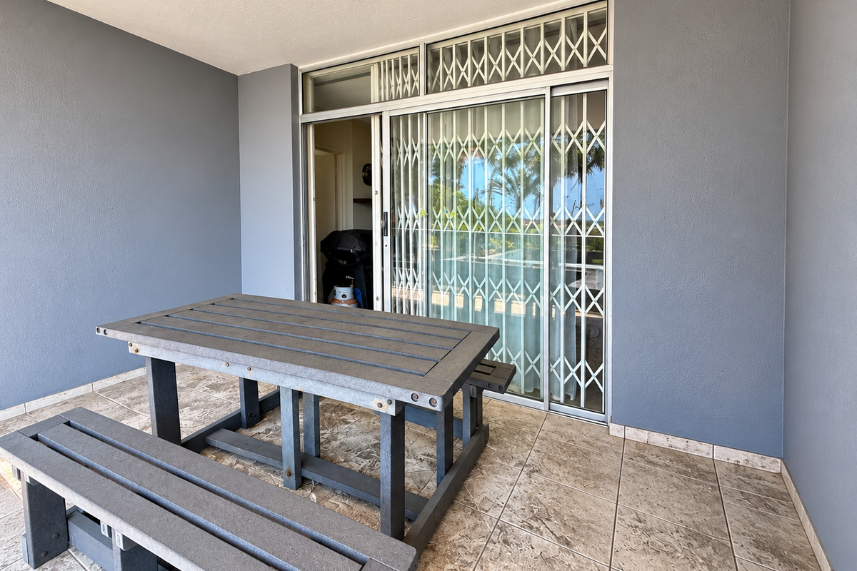 A covered patio area featuring tiled flooring, a sliding glass door with a security gate, and a skylight, providing a functional outdoor living space.